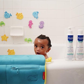 Young child taking a bath with mustela skin care products