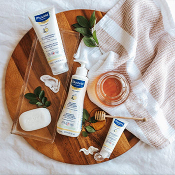 Mustela baby products on a wood round tray on bed