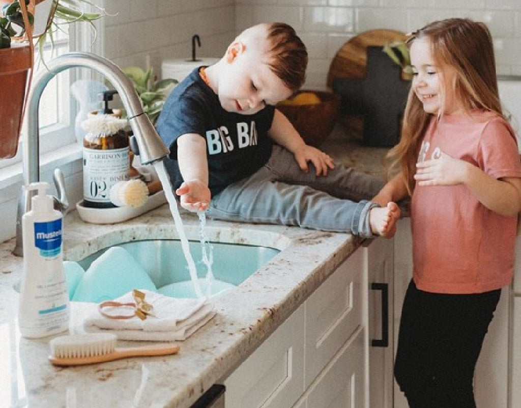 siblings washing hands in the kitchen sink