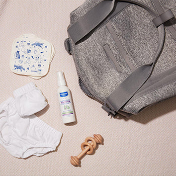 Diaper bag with baby items laid out on ground