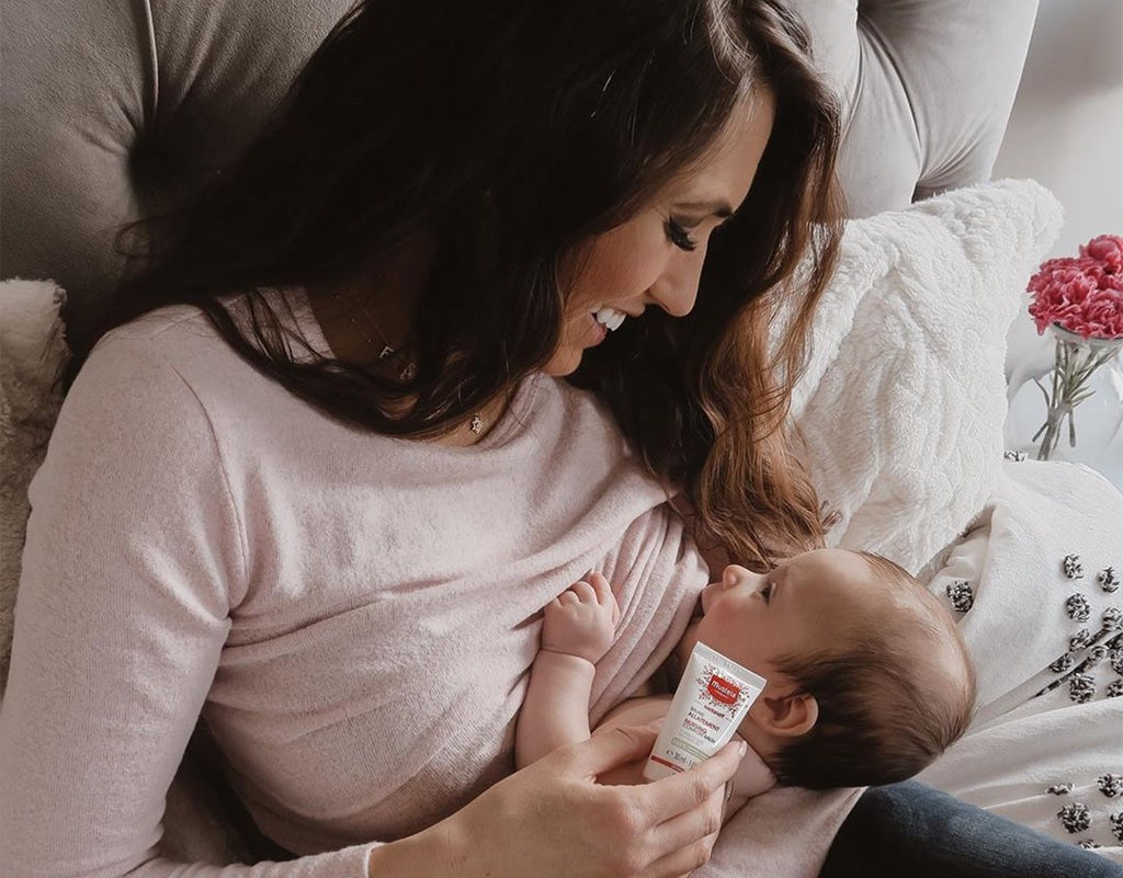 Mom breastfeeding newborn with essential breastfeeding supplies