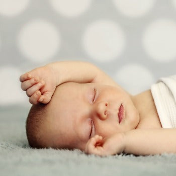 baby sleeping on back with hands above his head
