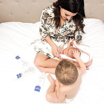 mother and child holding infant on bed with Mustela bath products