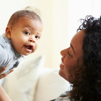 baby looking to the side as mother holds him up towards her