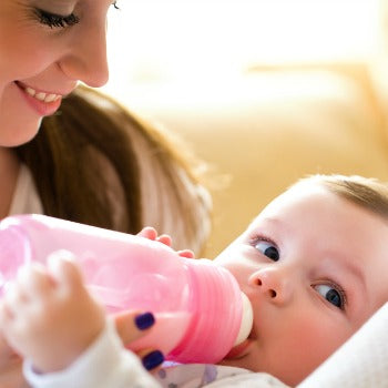 mother smiling at baby as she drinks from pink bottle