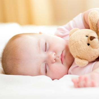 baby sleeping on her side while holding teddy bear