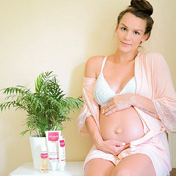 Smiling pregnant woman with Mustela products