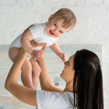 woman holding happy baby above her head on white background