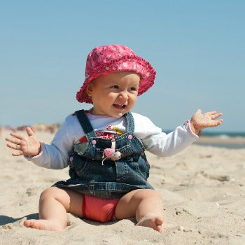 baby girl playing on a beach in sun hat