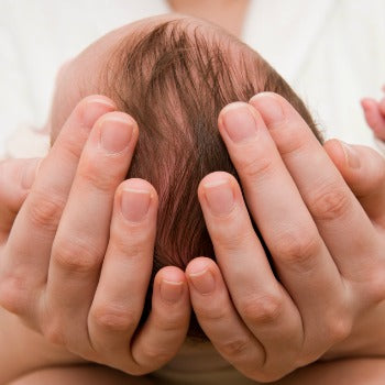 top of baby's head being cradled in mother's hands