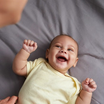 baby in gele onesie liggend op de rug en giechelend