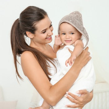 Mutter hält ihr Baby nach einem regelmäßigen Bad, das bei der Behandlung von trockener Kopfhaut helfen kann