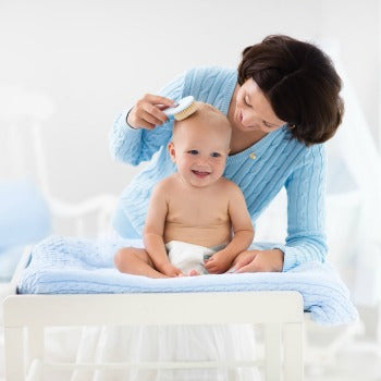 madre de pie detrás de un bebé feliz mientras le cepilla la cabeza