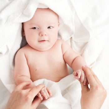 baby lying on white towels as parent holds both hands