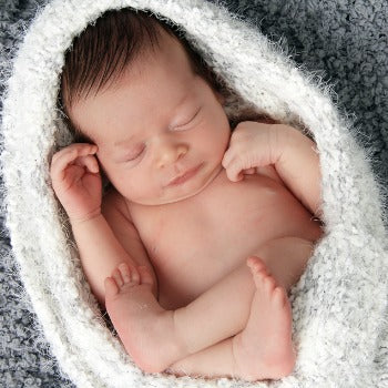newborn sleeping on back wrapped in knit blanket