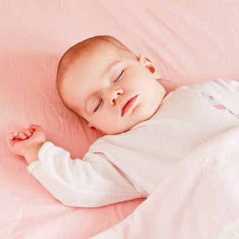 baby sleeping on pink sheet with one hand raised