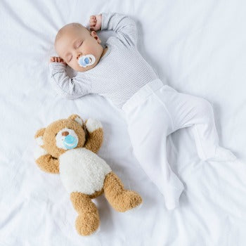 baby with pacifier in mouth sleeping next to a teddy bear