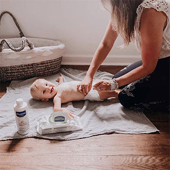 Woman changing baby on the floor using Mustela products