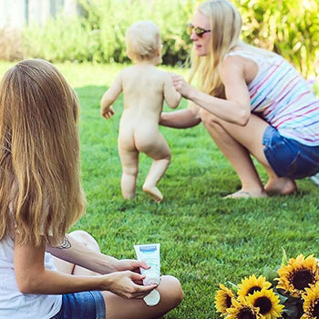 mother and girl playing with baby in grassy yard