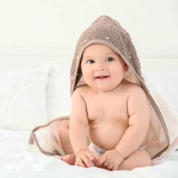 happy baby sitting in hooded towel after bath time