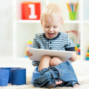 toddler giggling at tablet while sitting on potty chair 