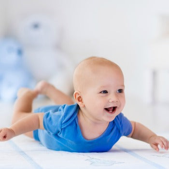 happy baby on his tummy, wearing a blue onesie