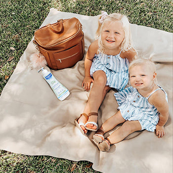 To toddlers on a blanket next to a diaper bag that's filled with diaper bag essentials