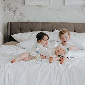 Two kids on a bed with Mustela skincare products with Emollients