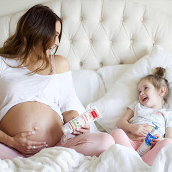 Mom with daughter in bed while applying mustela products on her belly