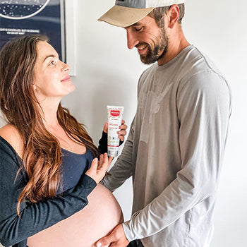 Man helping pregnant woman apply cream on her belly