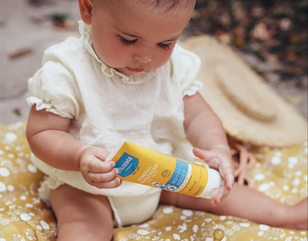 Baby holding Mustela Sunscreen with non-nano zinc oxide