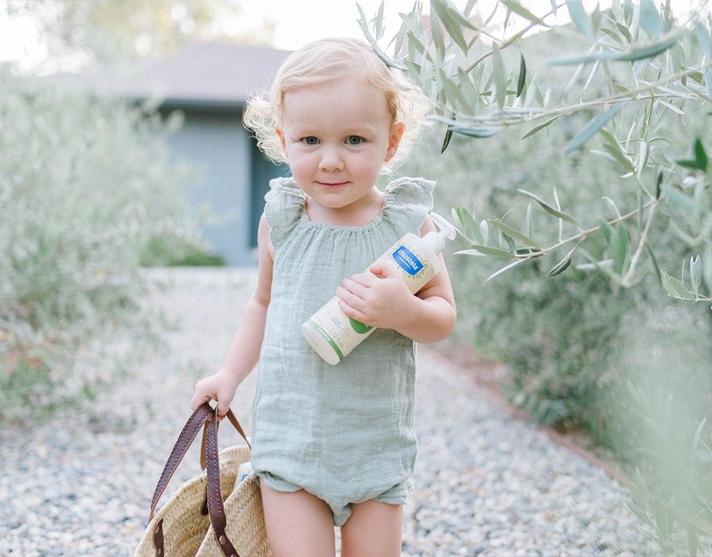 Little girl holding purse and mustela products that have Olive Oil For Skin