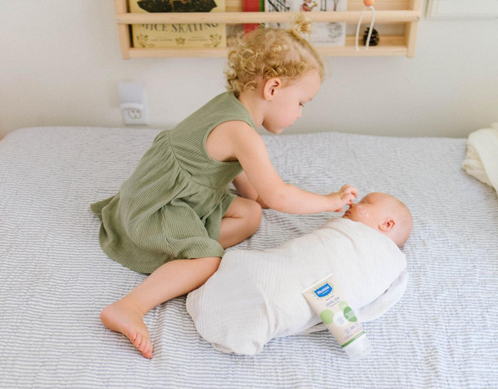 Sibling applying lotion with olive oil for skin on newborn baby