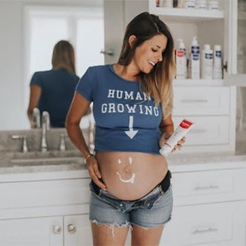 Woman with pregnant belly wearing a shirt that says human growing with an arrow