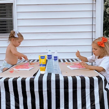 two kids painting outside while being protected by mustela sunscreen products