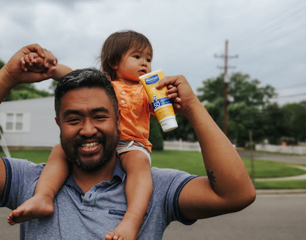 Dad holding kid on back while protecting him with sunscreen for sensitive skin