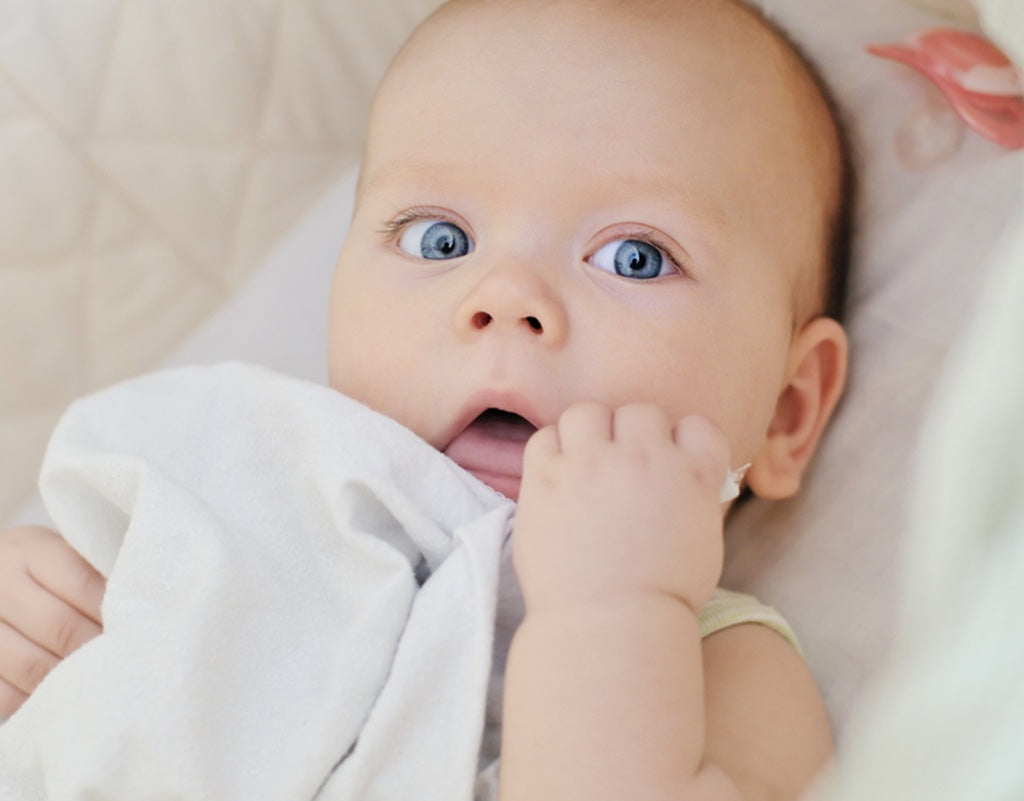 baby looking up at parent who is wondering when can baby sleep with blanket