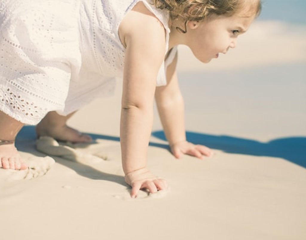 Parent takes child to the beach while wondering when do babies crawl
