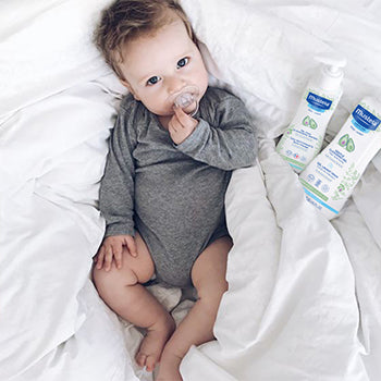 baby laying in crib with mustela products