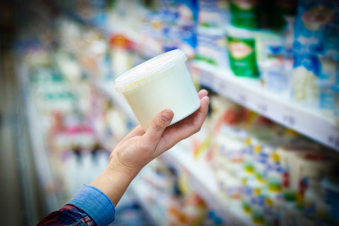 a hand holding a tub of sour cream in the dairy aisle