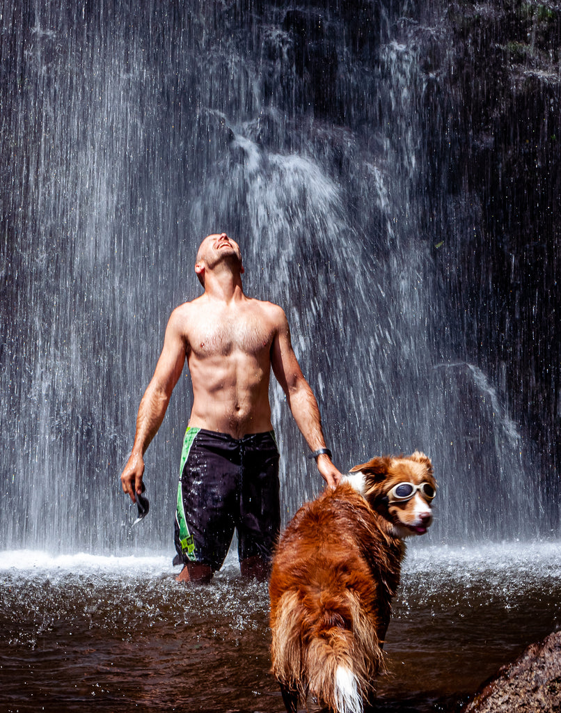 Dr. Dobias standing in a waterfall with his dog Skai 