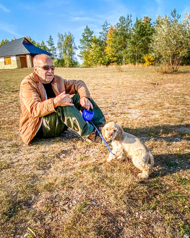 An old man sitting in a field with his Cocker Spaniel dog