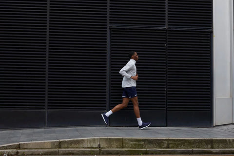 man running in white Castore jacket and navy shorts