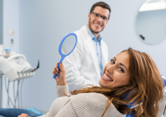 Women smiling in a dentist chair holding a mirror