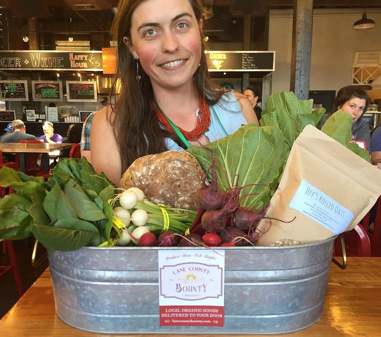 Shelley Bowerman smiles in front of a tub of artfully arranged vegetables with Lane County Bounty flyer