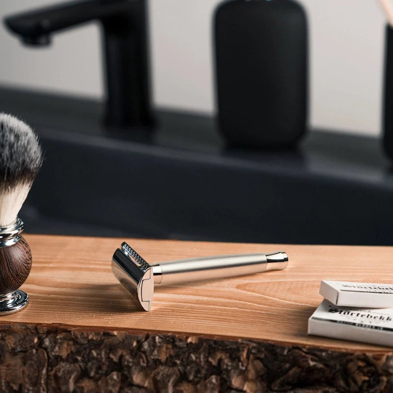 Men’s shaving razor and brush on a wooden surface with a speaker in the background.