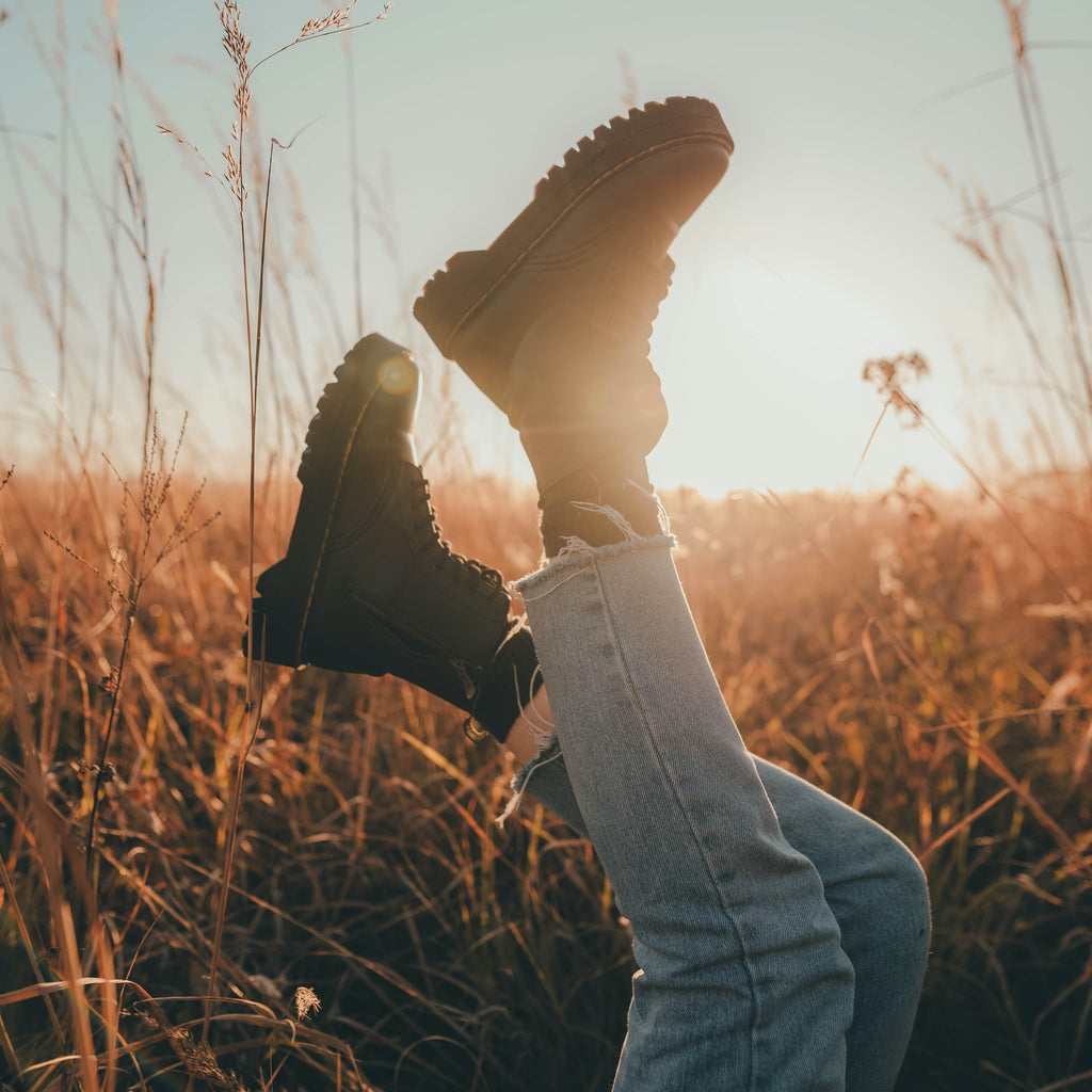 field background, showcasing someone's legs in jeans stretched upwards while wearing doc martens boots