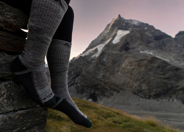 legs wearing wigwam socks in foreground with mountain in background at dawn or dusk