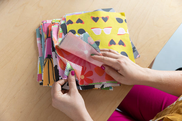 Hands-looking-through-a-stack-of-square-fabric-samples-on-a-table