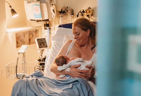 New mum in hospital bed after giving birth, breastfeeding and smiling at her newborn baby